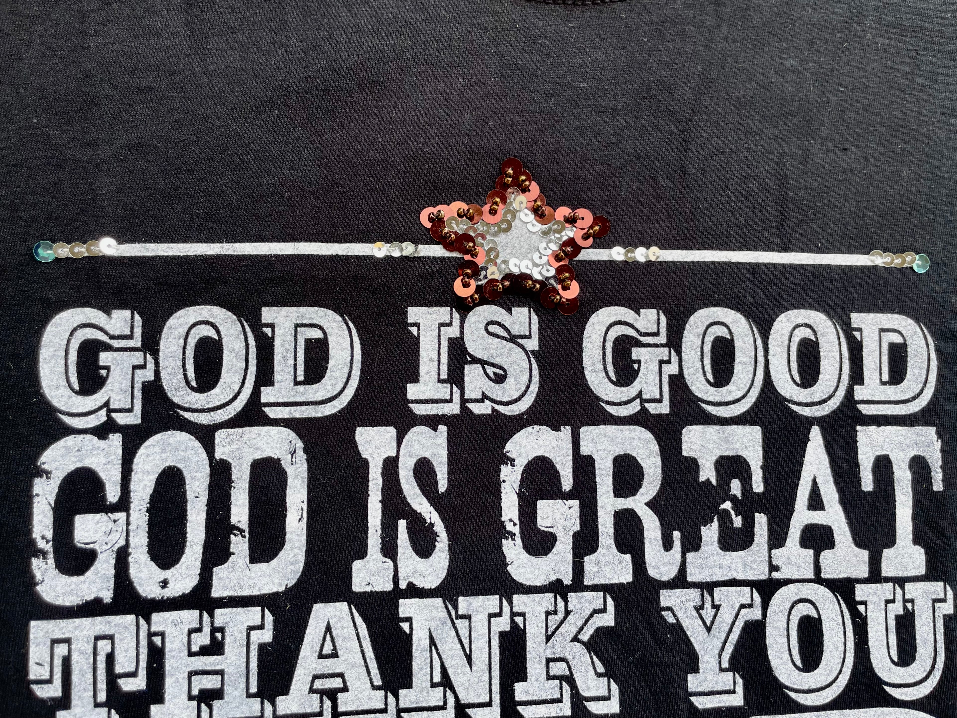 Black shirt with 'God is Good, God is Great, Thank You' text and decorative star brooch.