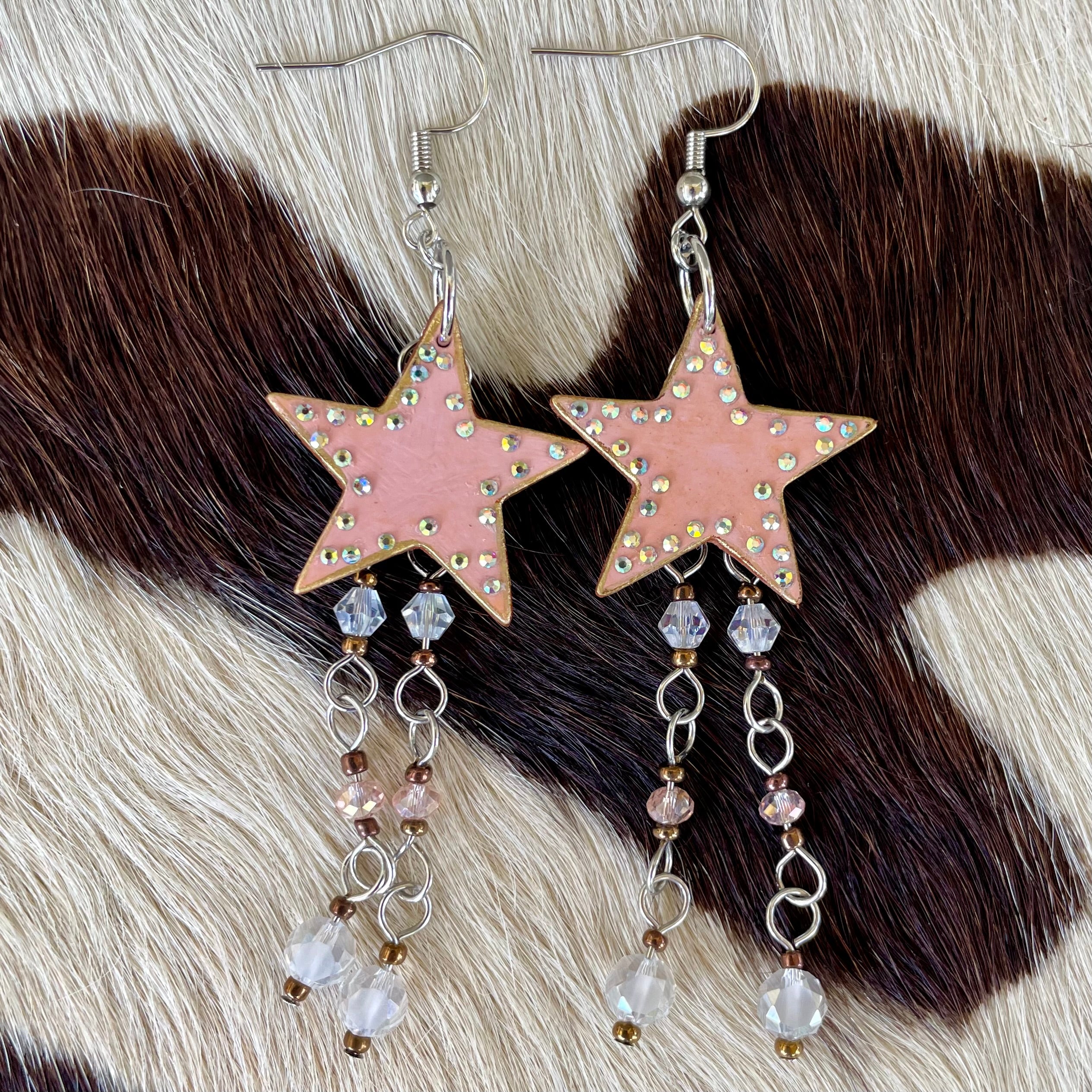 Star-shaped earrings with pink color and bead details on a fur background