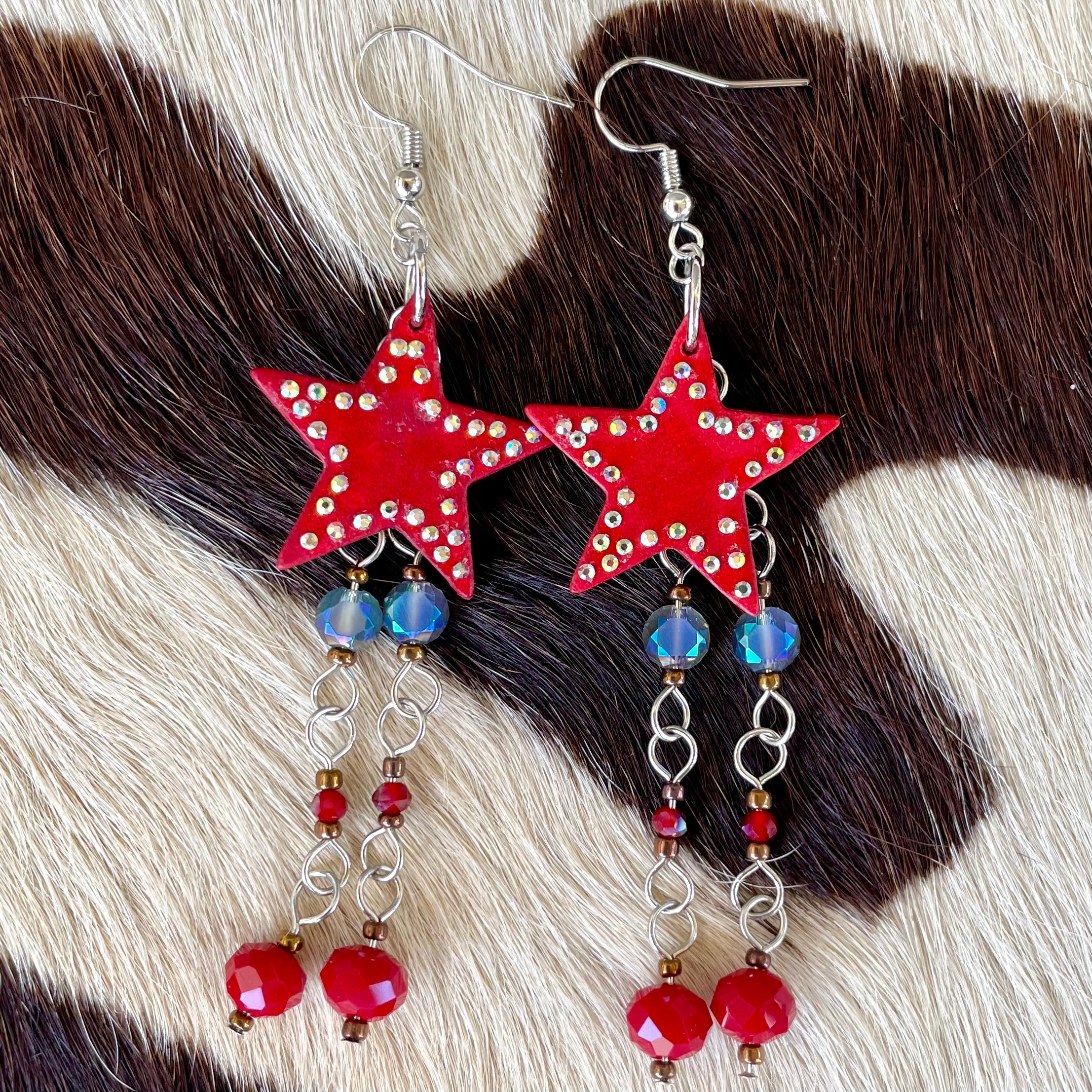 Red star-shaped earrings with bead details on a cowhide background
