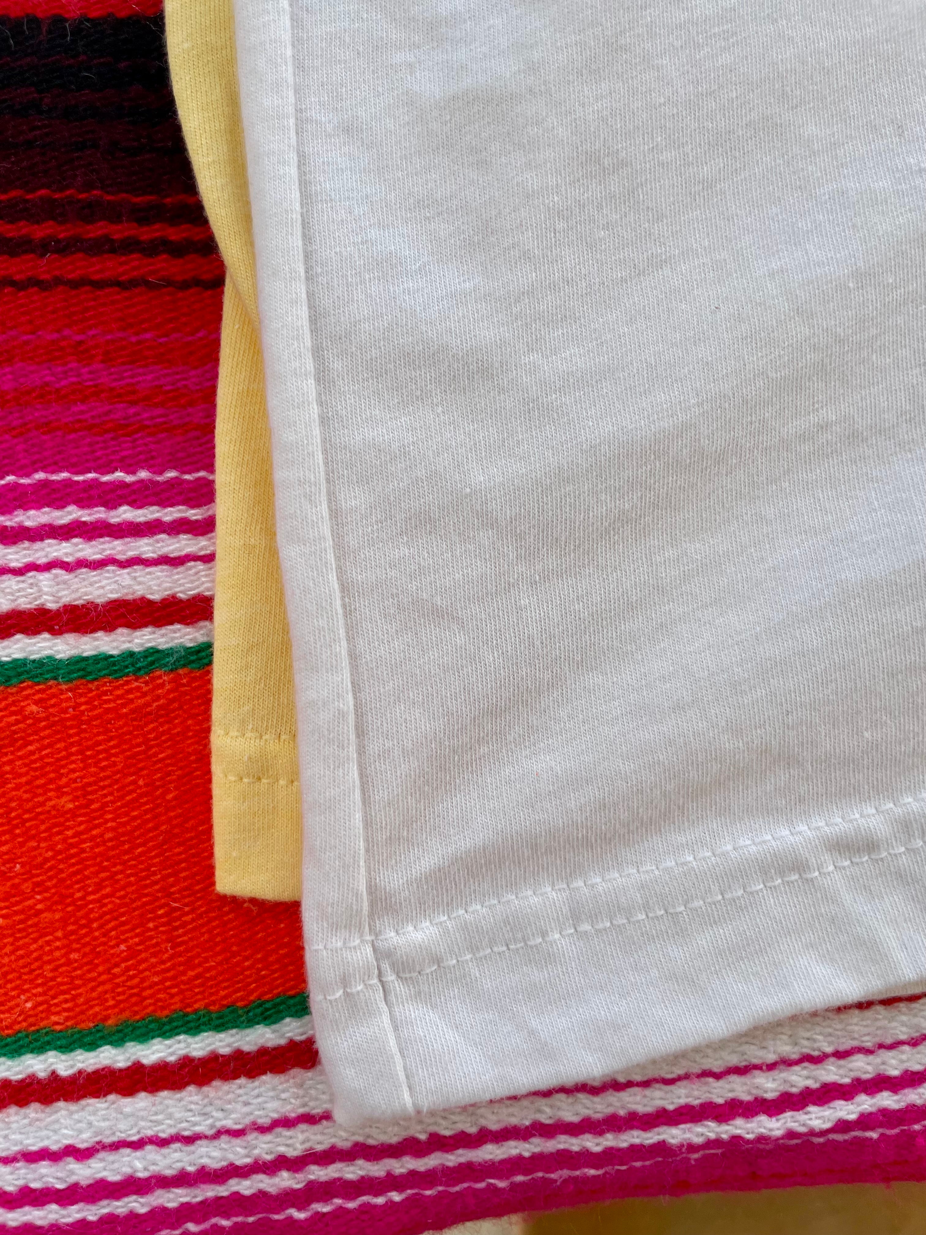 Yellow t-shirt with a graphic design of a woman in a hat and skirt, cactus, and sun on a colorful striped background.