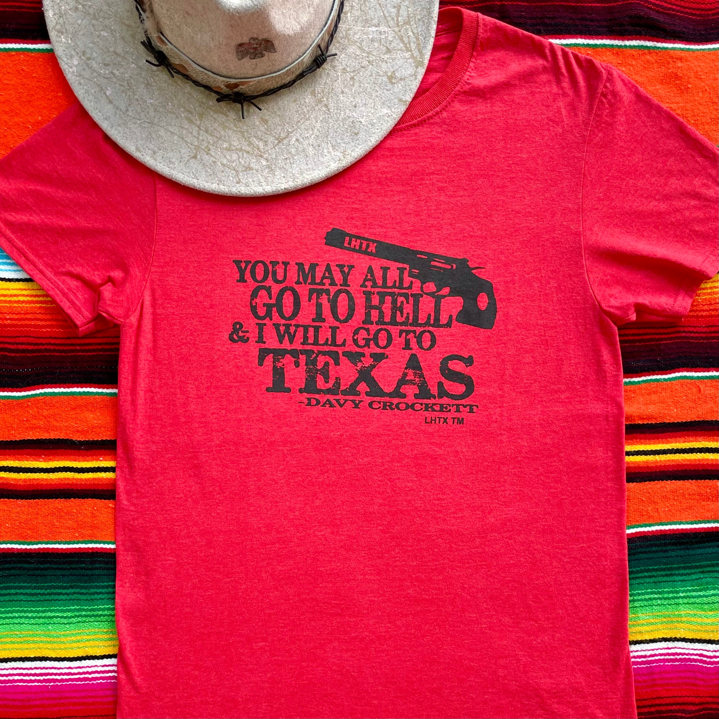 Red women’s graphic tee featuring Davy Crockett’s iconic quote “You may all go to hell and I will go to Texas.” Western slogan shirt rooted in Texas, designed by LHTX for bold southern style and patriotic pride. Hand drawn gun and screen printed. 