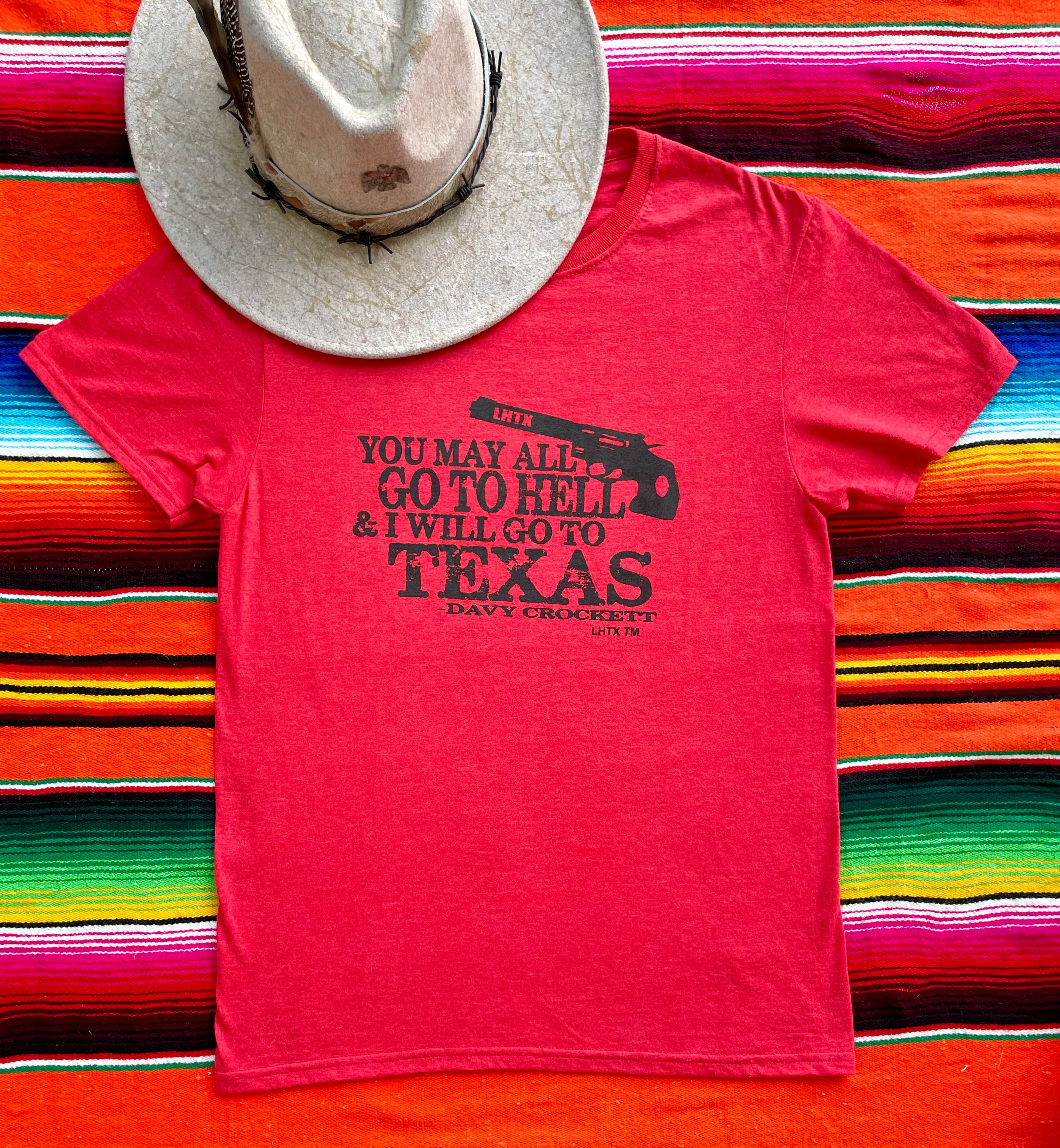 Red women’s graphic tee featuring Davy Crockett’s iconic quote “You may all go to hell and I will go to Texas.” Western slogan shirt rooted in Texas, designed by LHTX for bold southern style and patriotic pride. Hand drawn gun and screen printed. 