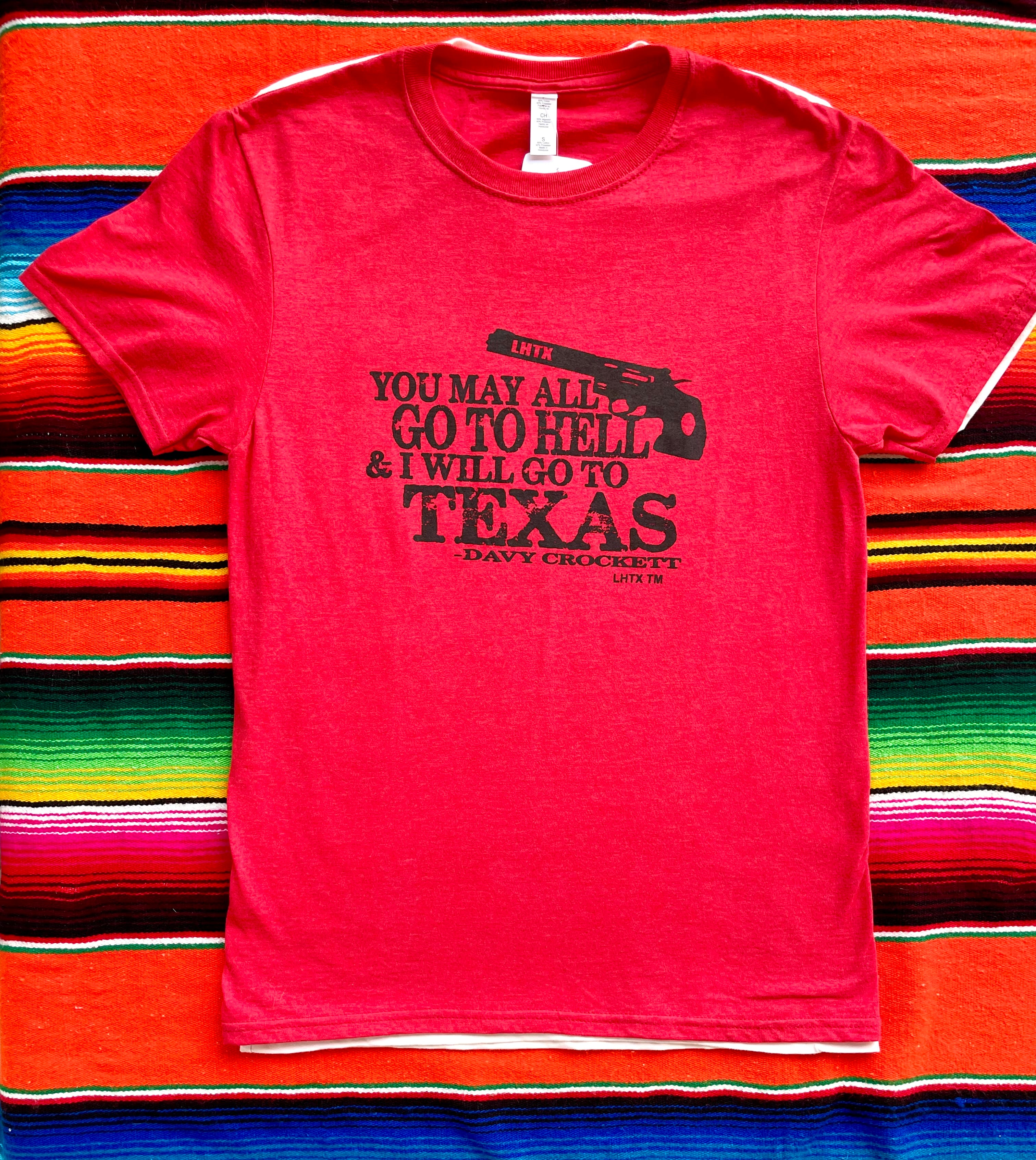 Red women’s graphic tee featuring Davy Crockett’s iconic quote “You may all go to hell and I will go to Texas.” Western slogan shirt rooted in Texas, designed by LHTX for bold southern style and patriotic pride. Hand drawn gun and screen printed. 