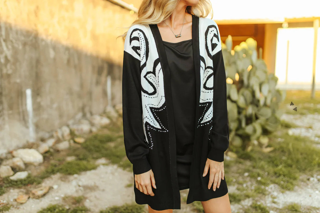 Person wearing a black dress with a white patterned cardigan in an outdoor setting.