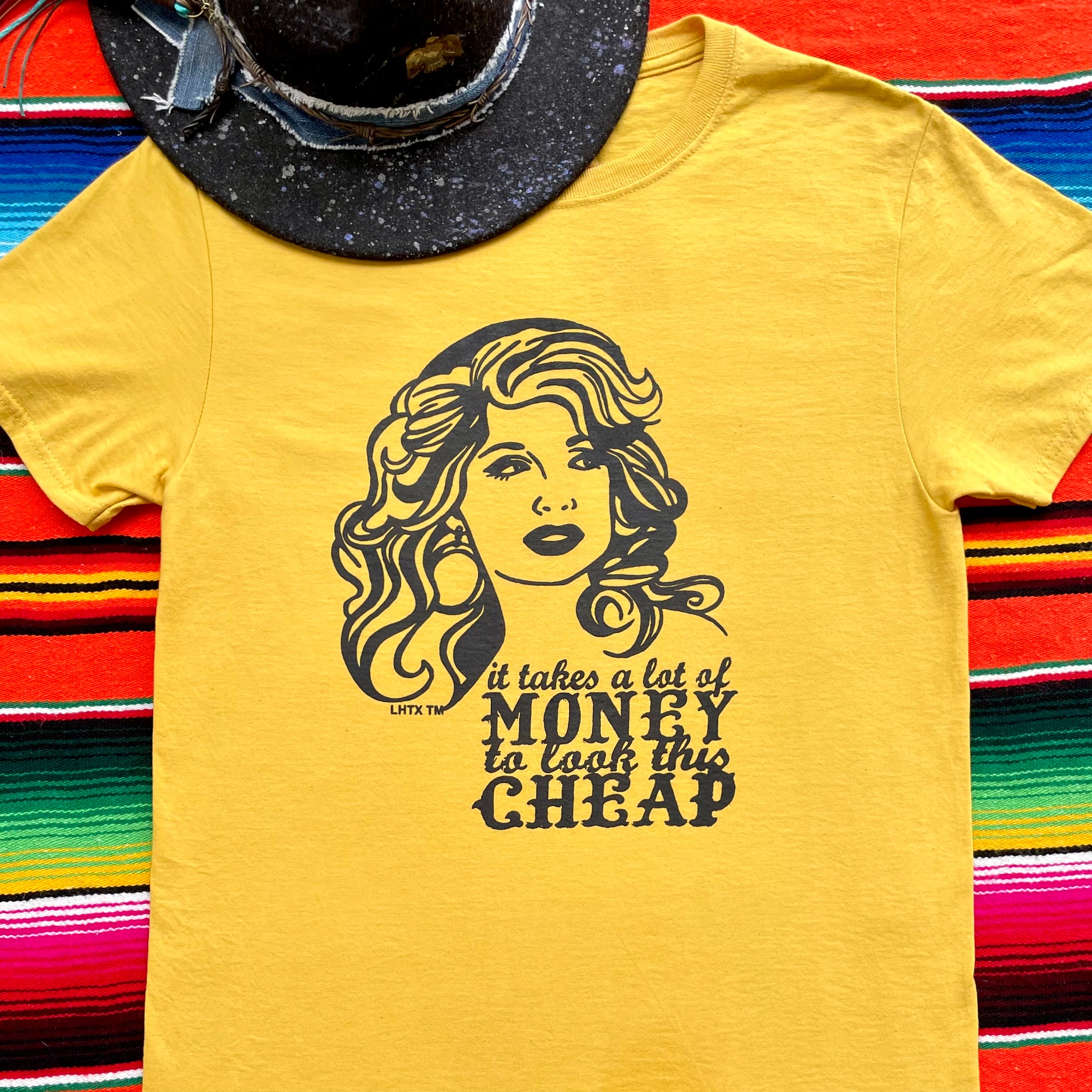 Dolly Parton quote graphic tee, "It takes a lot of money to look this cheap", with hand-drawn western design by LHTX, made in Texas—60% cotton, 40% polyester women’s t-shirt featuring bold southern charm and cowgirl style.”