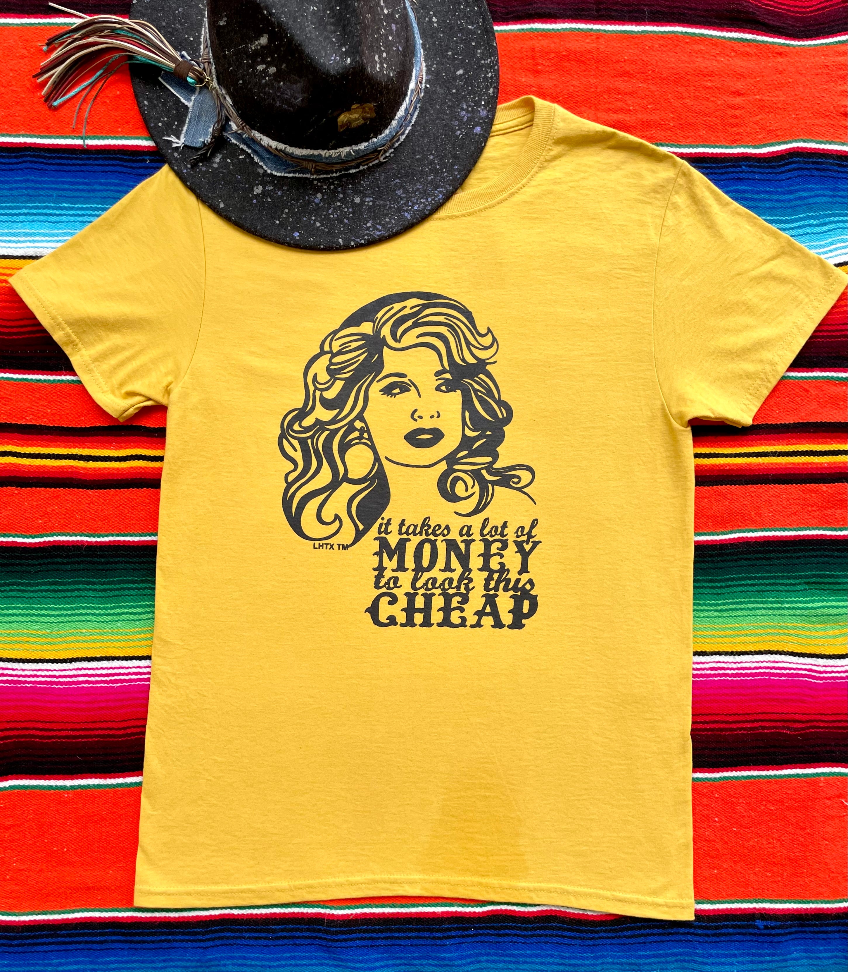 Mustard yellow Dolly Parton quote graphic tee, "It takes a lot of money to look this cheap", with hand-drawn western design by LHTX, made in Texas—60% cotton, 40% polyester women’s t-shirt featuring bold southern charm and cowgirl style.”